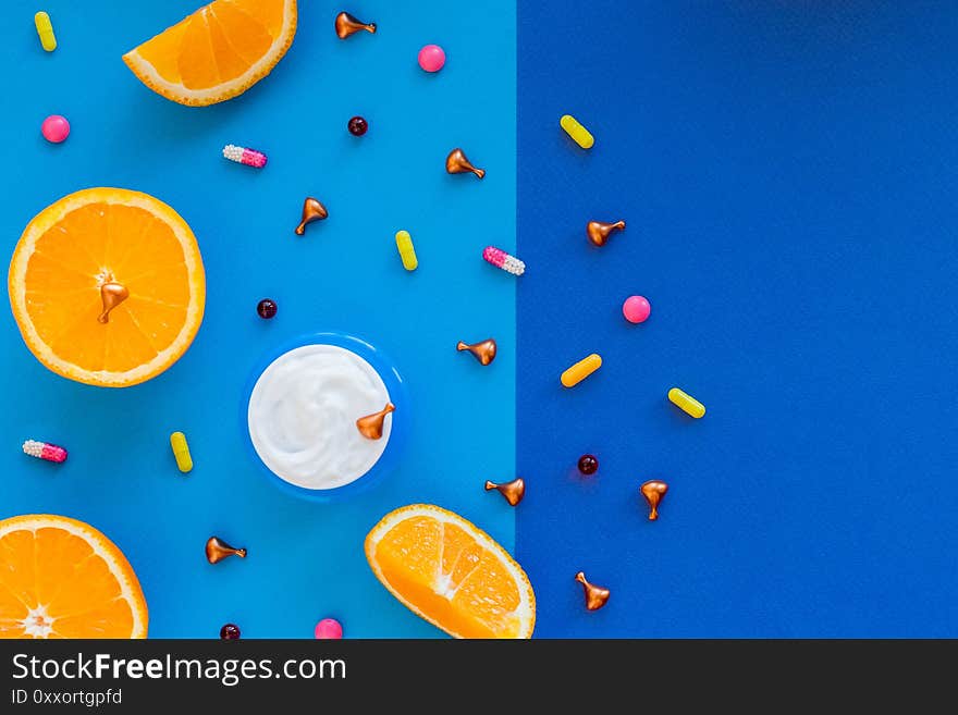 Vitamin C face serum with citrus slices, pills on blue background.golden capsules with face cream. cosmetics