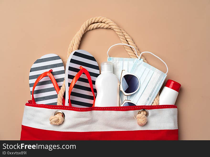 Beach bag with beach items and medical protective mask on beige background. Coronavirus summer concept