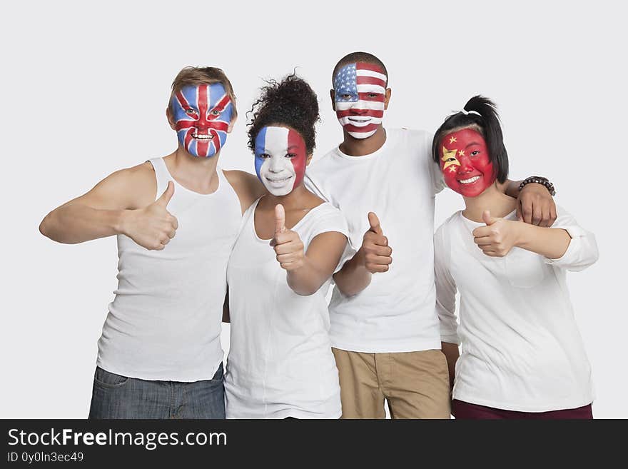 Photo of happy Multi-ethnic group of friends with various national flags painted on their faces gesturing thumbs up against white background