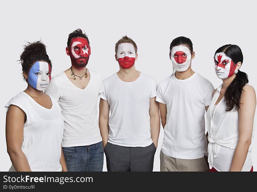 Portrait of serious Multi-ethnic group of friends with various national flags painted on their faces standing against white backgr