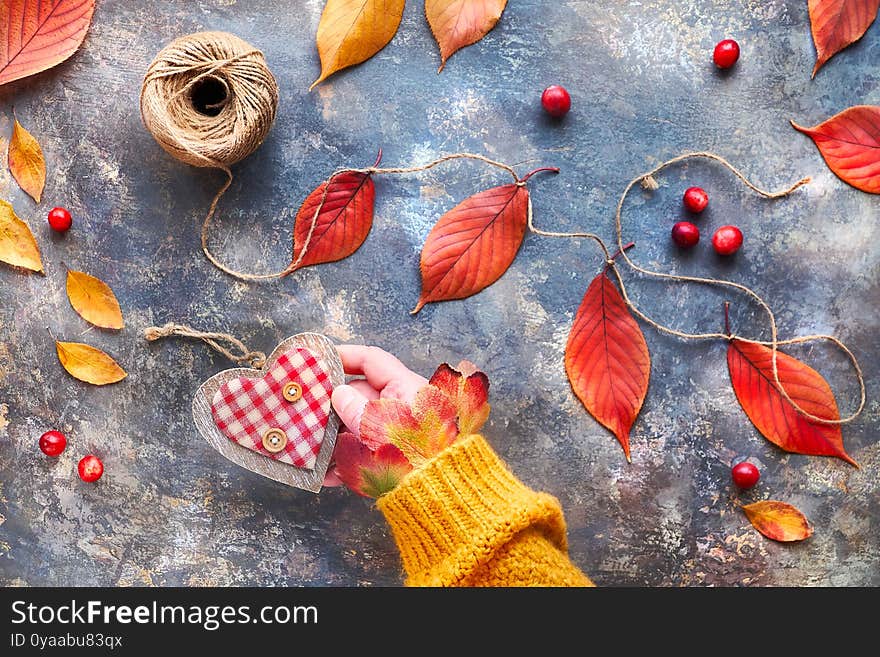 Hand In Orange Sweater Holds Wooden Heart. Natural Fall Decorations, Vibrant Red, Yellow Oak Leaves. Charity Campaign Concept