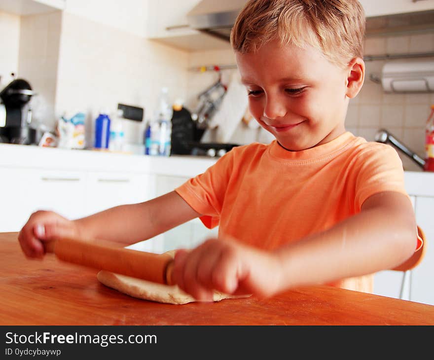 Blond hair little boy enjoys making pizza in the kitchen