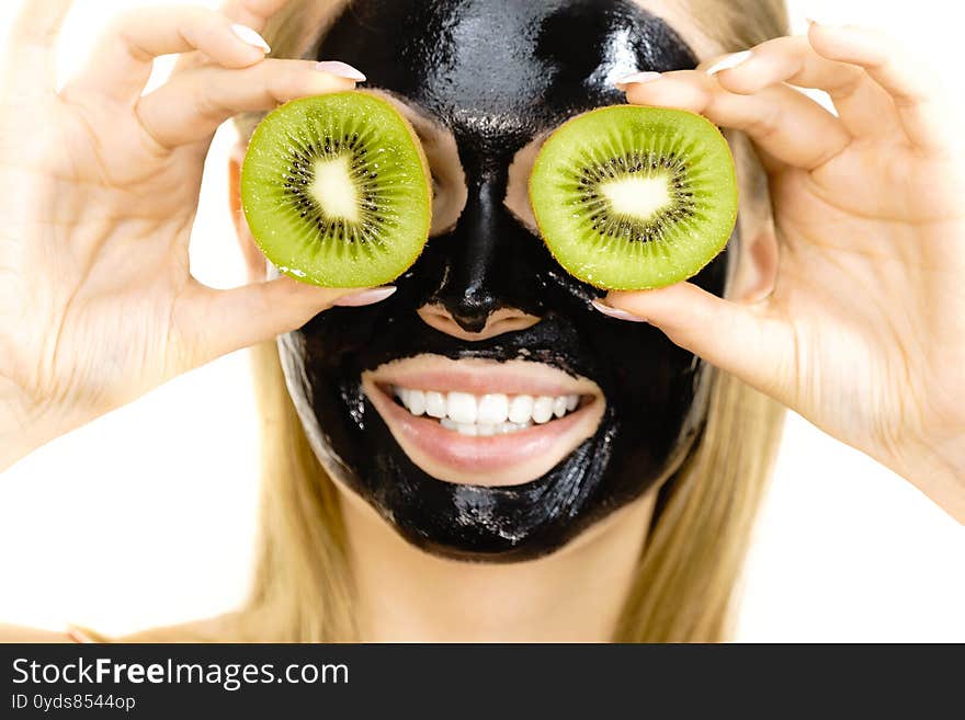 Young woman with carbo black peel-off mask on her face holding kiwi fruit halves, covering eyes, on white. Beauty treatment. Skincare. Young woman with carbo black peel-off mask on her face holding kiwi fruit halves, covering eyes, on white. Beauty treatment. Skincare