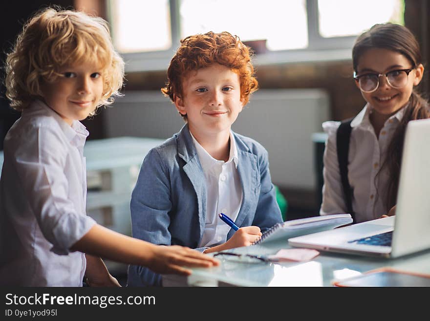 At school. Three cute kids studying in the classroom and looking happy