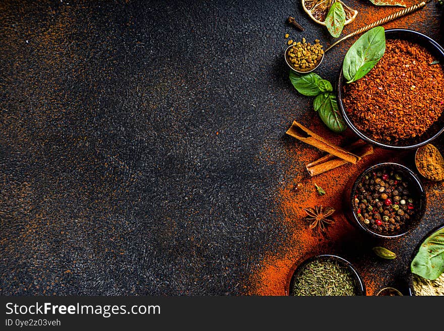 Set of Spices and herbs for cooking. Small bowls with colorful  seasonings and spices - basil, pepper, saffron, salt, paprika, turmeric. On black stone table top view copy space