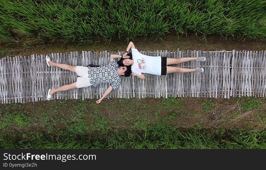 Asian couple lay down on wooden path in green rice field. aerial view of bamboo walk way with people. Nan, Thailand.