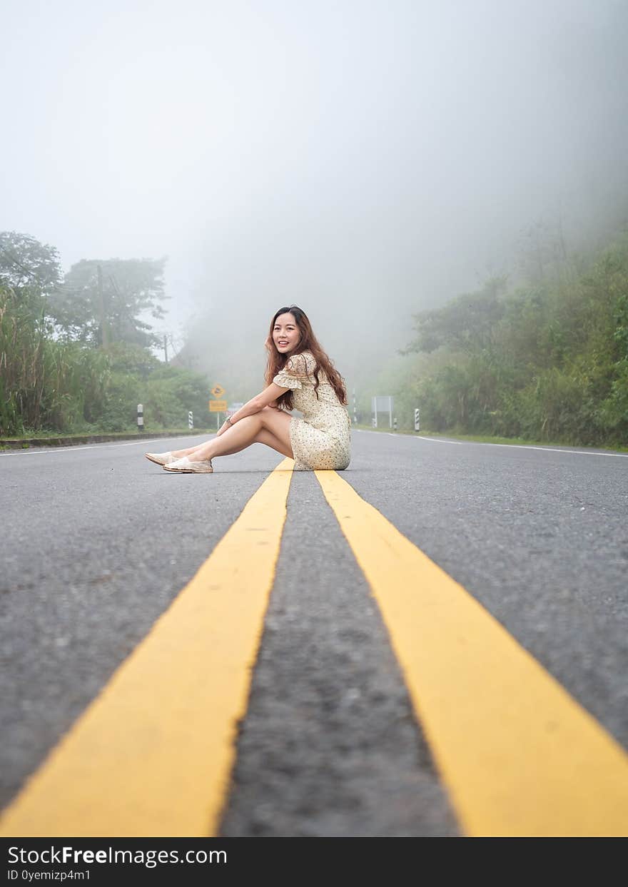 Asian Woman Sitting On Road Center Line. Road On Mountain In Foggy Day.