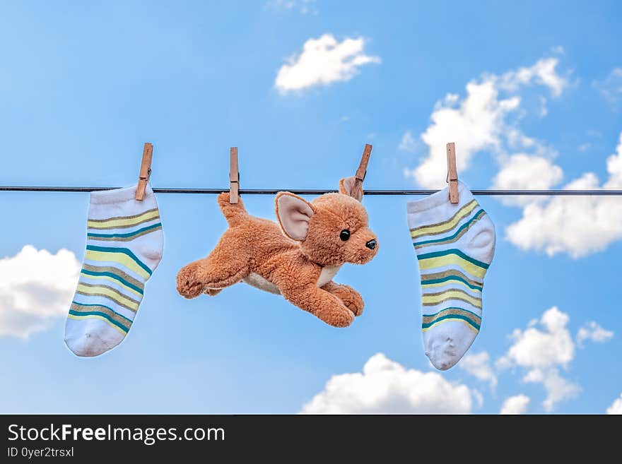 Soft toy and striped socks dry on a clothesline against a blue sky with white clouds, laundry concept, clean clothes after washing. Soft toy and striped socks dry on a clothesline against a blue sky with white clouds, laundry concept, clean clothes after washing