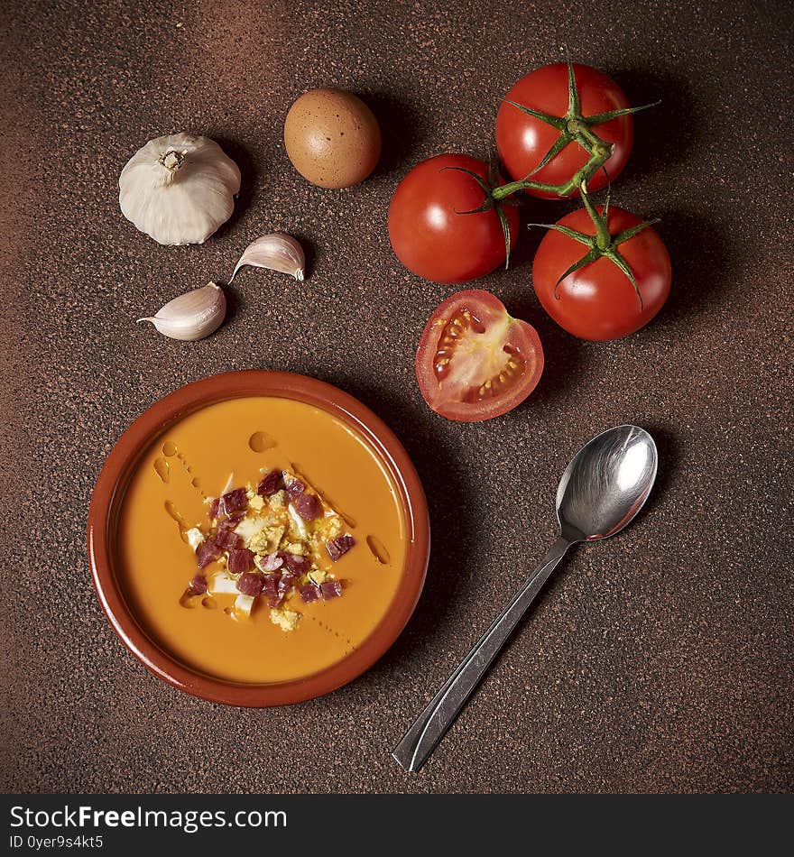 An earthenware bowl with spanish salmorejo, tomatoes, garlic, eggs and ham over a rustic wooden table. An earthenware bowl with spanish salmorejo, tomatoes, garlic, eggs and ham over a rustic wooden table