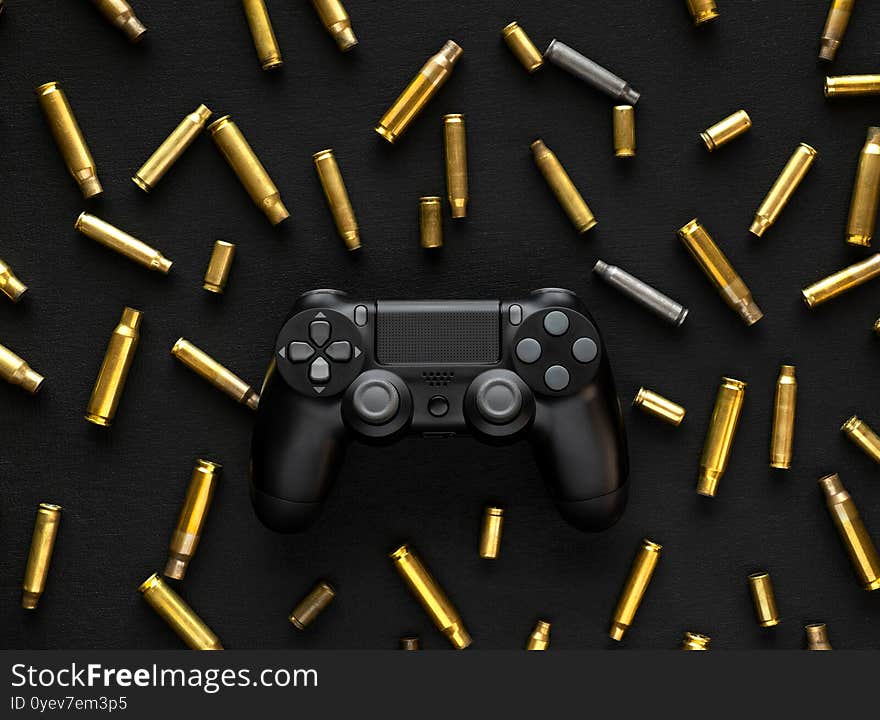 Modern black gamepad on a black background among the spent cartridges. Game concept. Shooter game