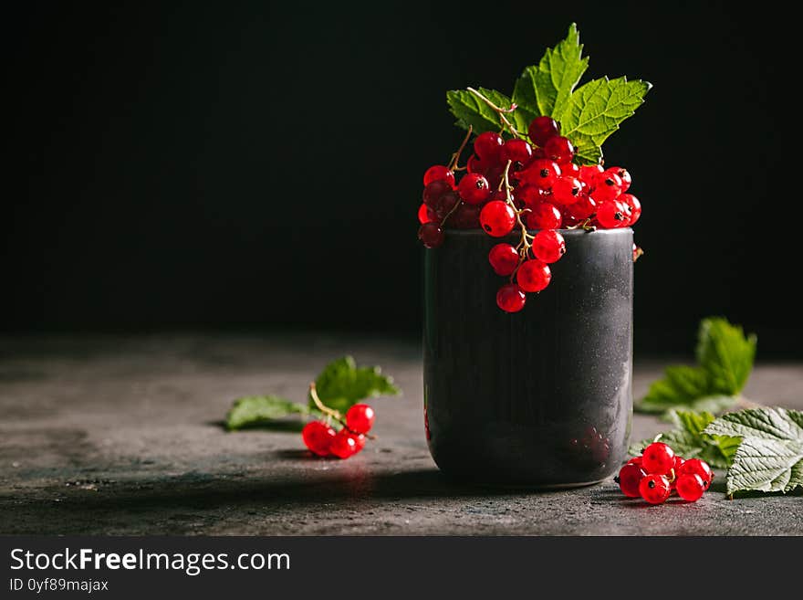 Red currant with leaves in a gray ceramic cup on a gray background