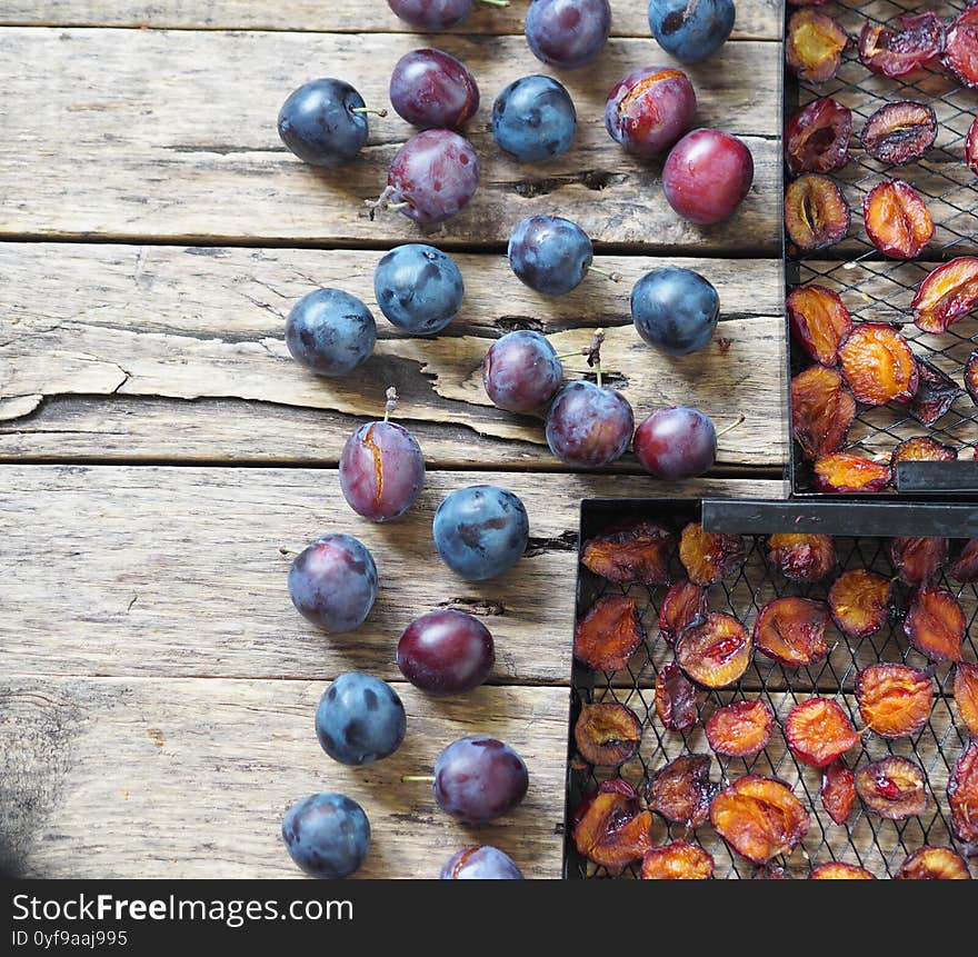 Black grates from a home fruit and vegetable dryer with dried plums on a wooden background with fresh plums. Home preparation of