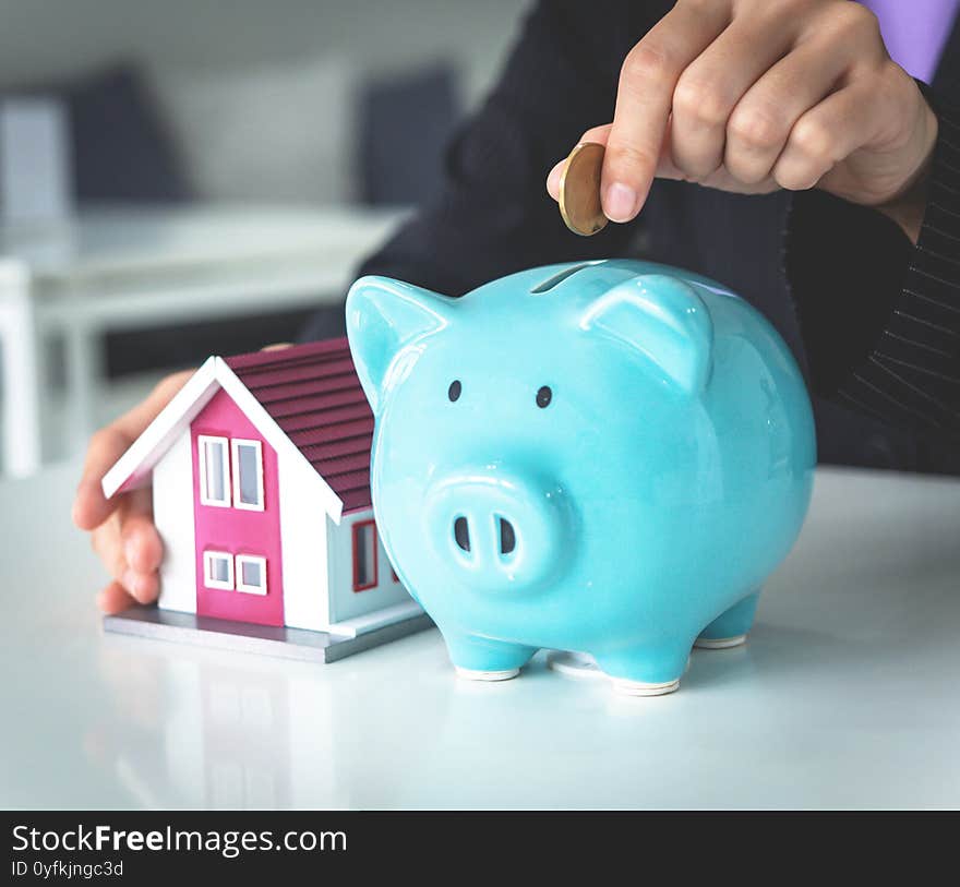 Business woman is putting money in to piggy bank, saving money to invest in hose, business financial concept. copy-space in white background,