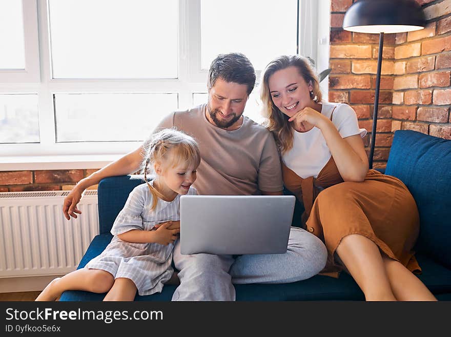 Caucasian family sit using laptop on sofa at home, they look at screen of modern laptop, watch videos, movies, news. family concept