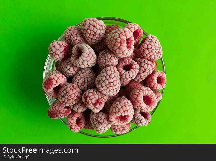 Frozen raspberries in a plate on a bright green background. View from the top.