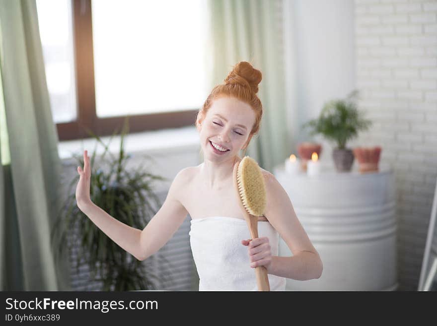 Vivacious emotional young woman with red hair bun taking bath at home, being in good temper, singing a song holding body brush as a microphone, giving way to her talant and joy. Vivacious emotional young woman with red hair bun taking bath at home, being in good temper, singing a song holding body brush as a microphone, giving way to her talant and joy