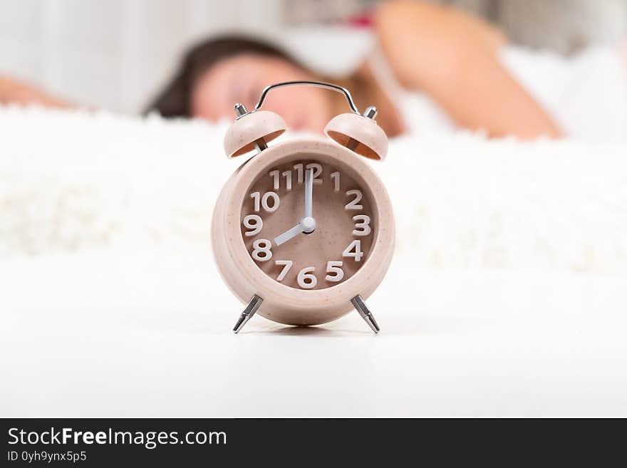 Alarm clock on the table in the bedroom. Peaceful model trying to wake up lying on her bed, selective focus. copy space. The concept of sleep, daily routine, start of a new day. High quality photo