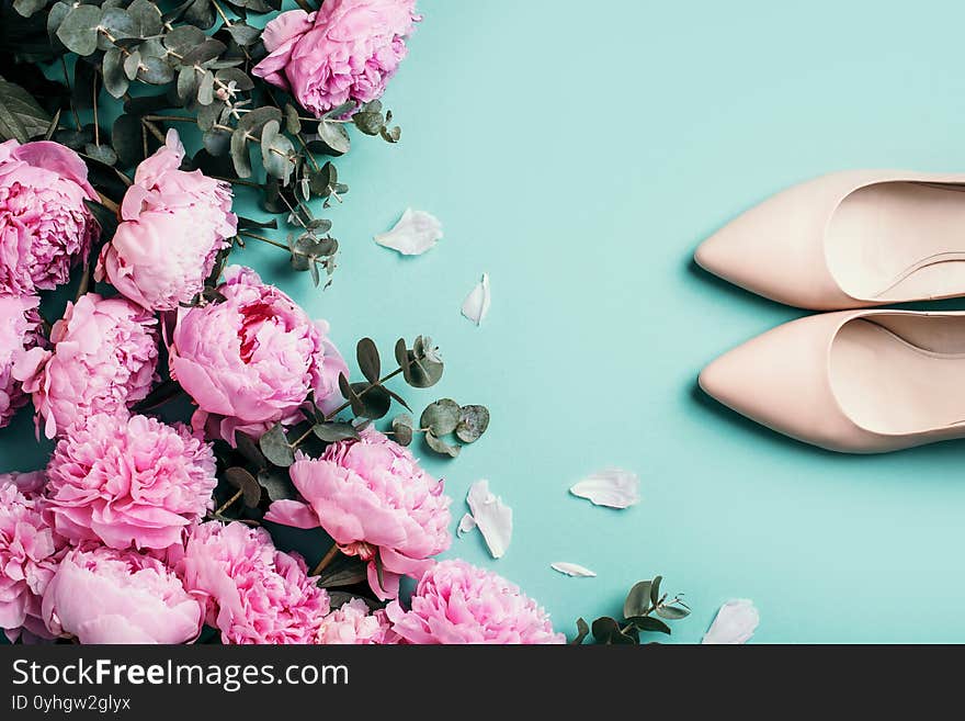 Woman nude shoes, pastel pink peonies, eucalyptus flowers on pastel blue background. Flat lay, top view. Copy space. Floral mock up. Wedding, birthday, anniversary bouquet. Woman day, Mother`s day