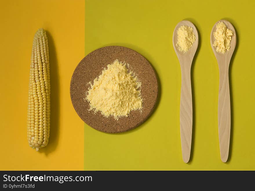 Corn flour on wooden spoons and a board, fresh corn on a double yellow green background. The concept of the production of products from corn. Top view