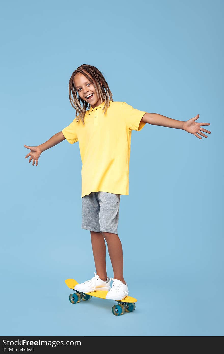 Gleeful Little Boy With African Dreads On Skateboard Having Fun Over Blue Background.