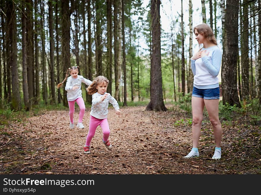 Mother and her child sister girls playing and having fun together on walk in forest outdoors. Happy loving family posing on nature landscape with with pine trees