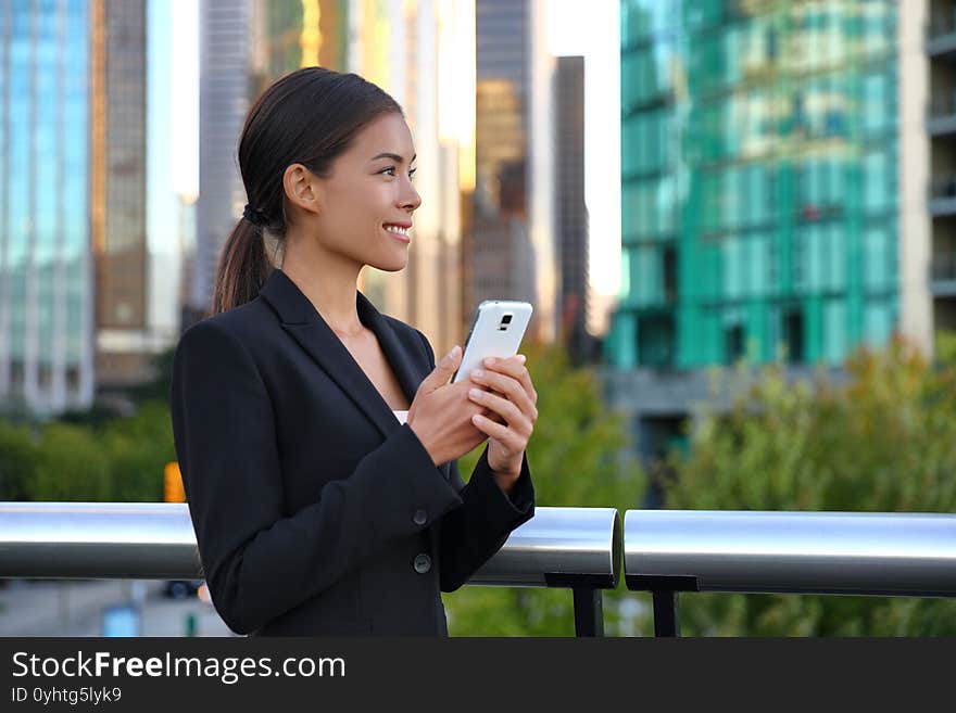 Phone Asian business woman in suit outside texting on mobile smartphone. Happy smiling businesswoman realtor working using smart phone. Young multiracial chinese caucasian lady at work.