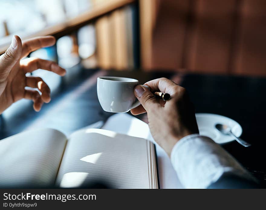 A man holds in his hand a cup of coffee pen books documents cafe. High quality photo