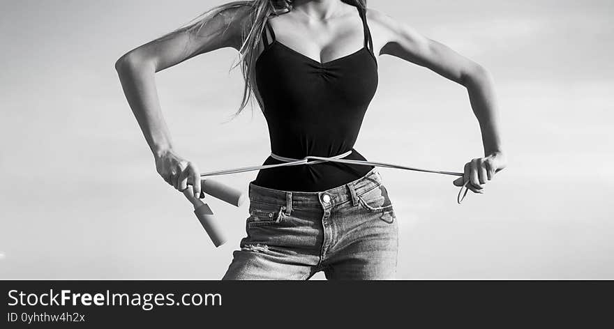 Girl with perfect waist with a jump rope in hands. Athletic slim woman measuring her waist by measure tape after diet. Fit fitness girl measuring her waistline with measure tape. Black and white.