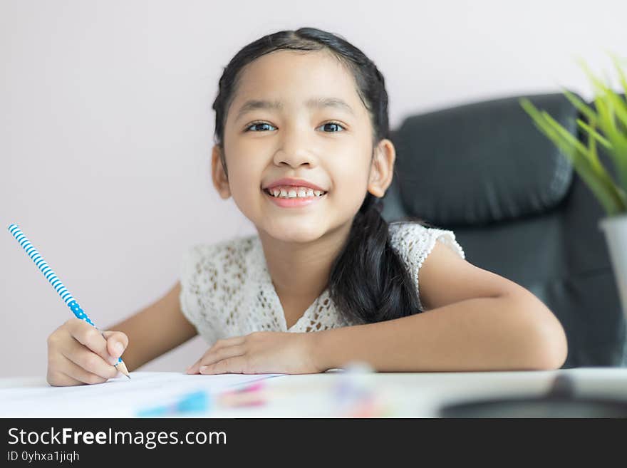 Little Asian girl using the pencil to write on the paper doing homework and smile with happiness for education concept select