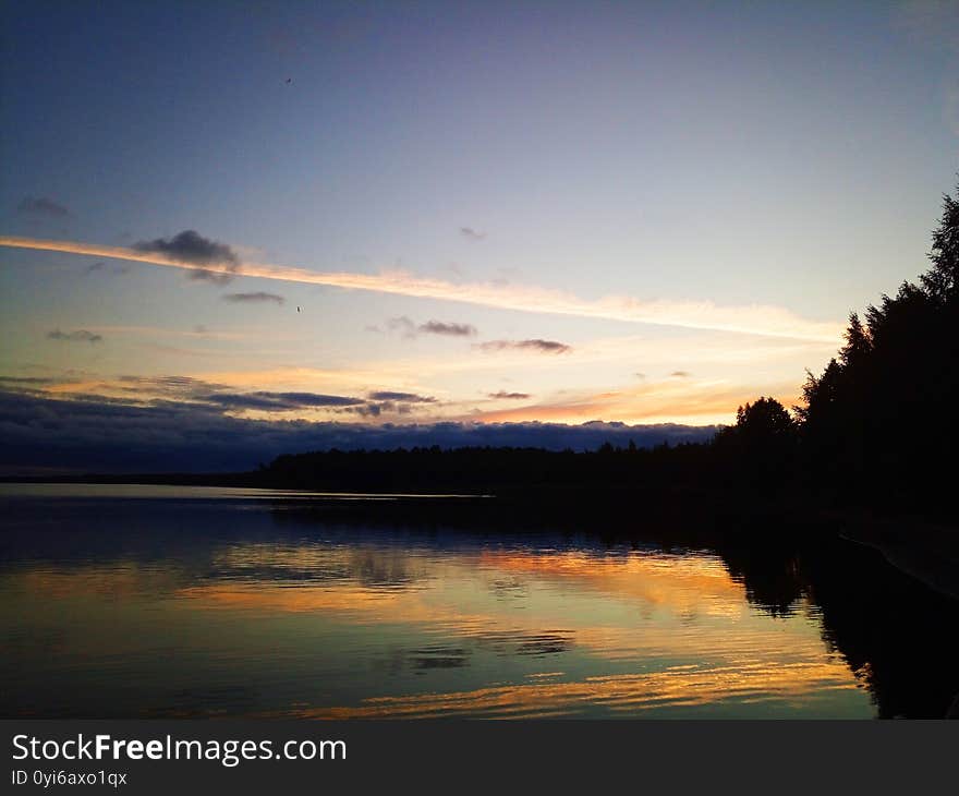 Lake reflects sky. Yellow colored sunset. Dark blue clouds. Marks made by planes can be seen. Horizon over lake. Tree silhouettes. Rekyvos ezeras. Lake reflects sky. Yellow colored sunset. Dark blue clouds. Marks made by planes can be seen. Horizon over lake. Tree silhouettes. Rekyvos ezeras.