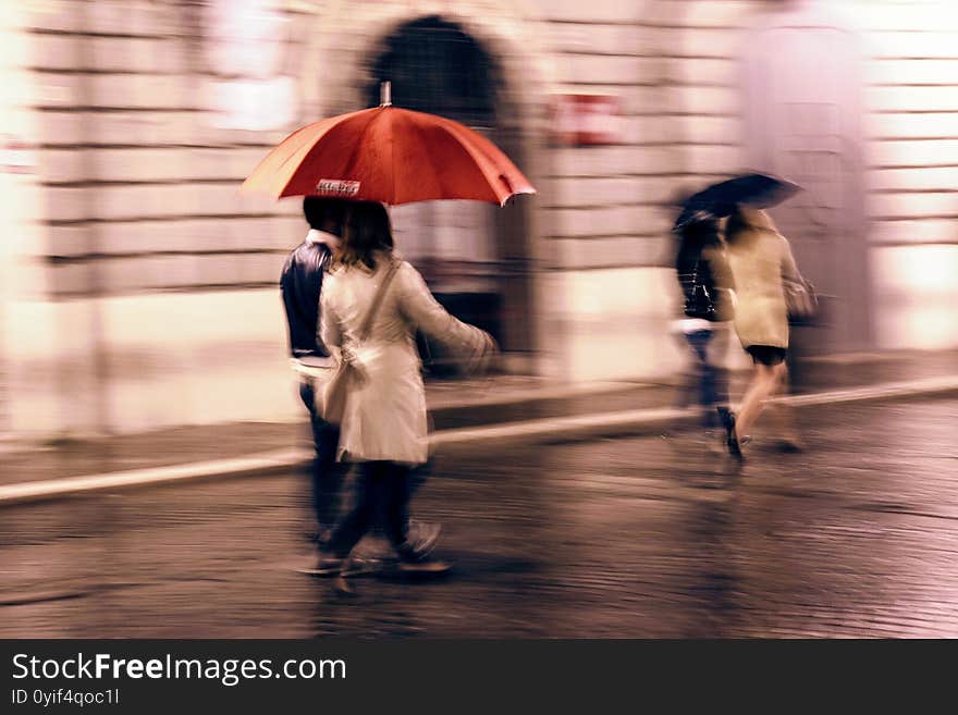 Motion blurred abstract image of people under red umbrella walking in the rain. Motion blurred abstract image of people under red umbrella walking in the rain.