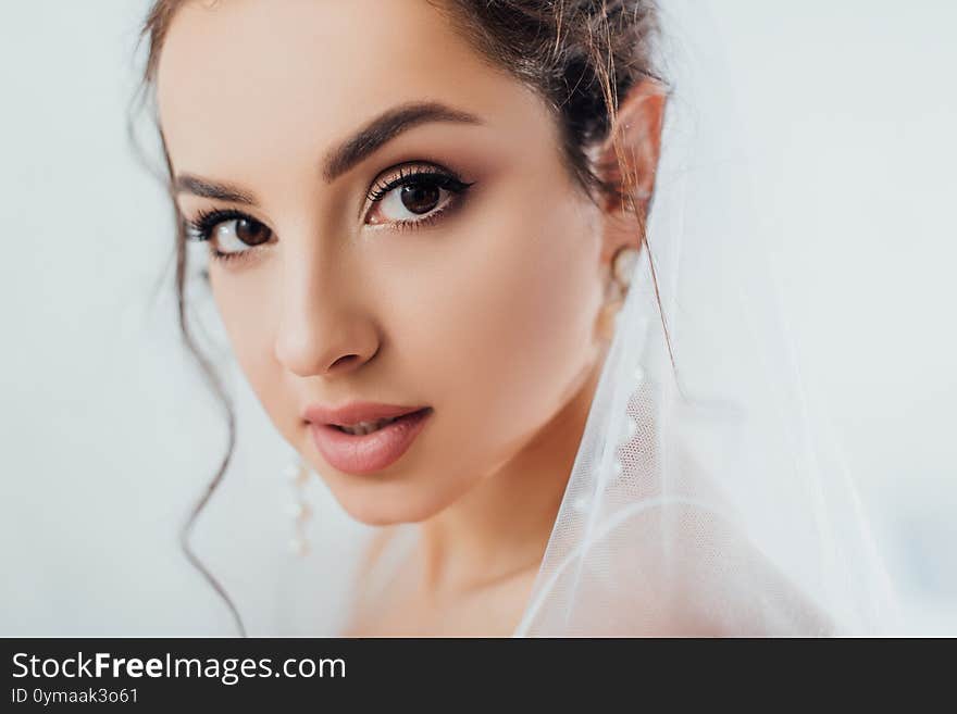 Selective focus of brunette bride in pearl earrings and veil looking at camera