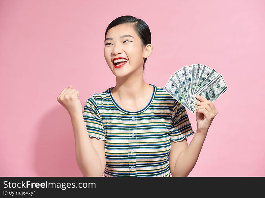 Portrait Of A Cheerful Young Woman Holding Money Banknotes And Celebrating Isolated Over Pink Background