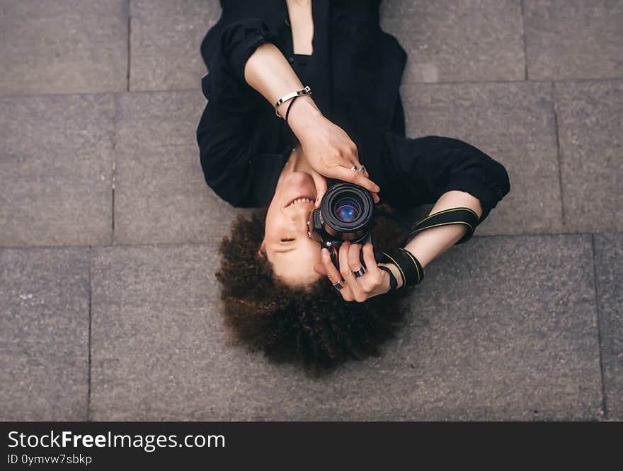 Brunette woman with digital 50mm lens reflex camera is lying on the steps. Top view