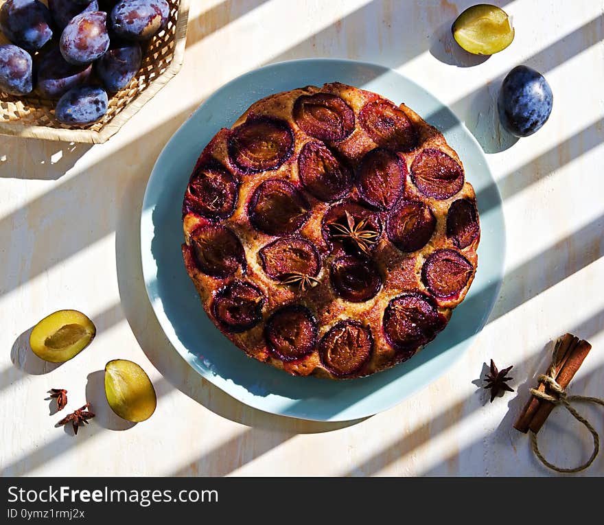 Round honey cake or muffin with fresh plums on a turquoise teatka on a light concrete background. Plum baked goods