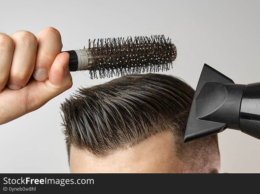 Man styling his hair with hair dryer and round brush. Hair care at home after barbershop. Mans fashion and modern haircut