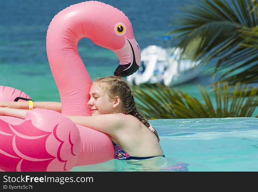 Caucasian teenage girl hugging her inflatable pink flamingo in infinity swimming pool in luxury hotel, Punta Cana, Dominican Republic. Summer vacation concept. Caucasian teenage girl hugging her inflatable pink flamingo in infinity swimming pool in luxury hotel, Punta Cana, Dominican Republic. Summer vacation concept