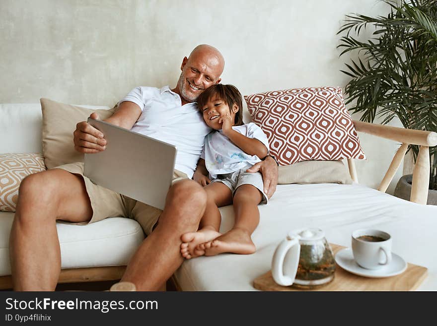 Father And Son With Tablet Portrait. Mixed Race Family Of Dad And Little Boy Using Portable Digital Device Sitting On Sofa Together. Technology For Education And Fun At Tropical Resort. Father And Son With Tablet Portrait. Mixed Race Family Of Dad And Little Boy Using Portable Digital Device Sitting On Sofa Together. Technology For Education And Fun At Tropical Resort.