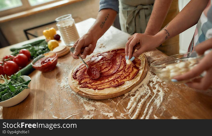 Team work. Cropped shot of couple making pizza together at home. Man in apron adding, applying tomato sauce on the dough while women adding mozzarella cheese. Selective focus. Web Banner