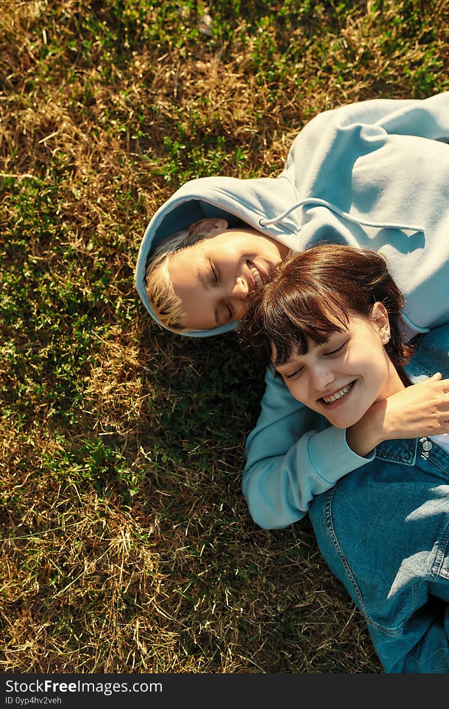 Top view of happy lesbian couple of girls lying on the grass in summer park, women in love laughing, spending time together outdoors, relationships and LGBT concept