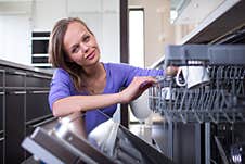 Pretty, Young Woman In  Kitchen Putting Cups Into The Dishwasher Stock Photos