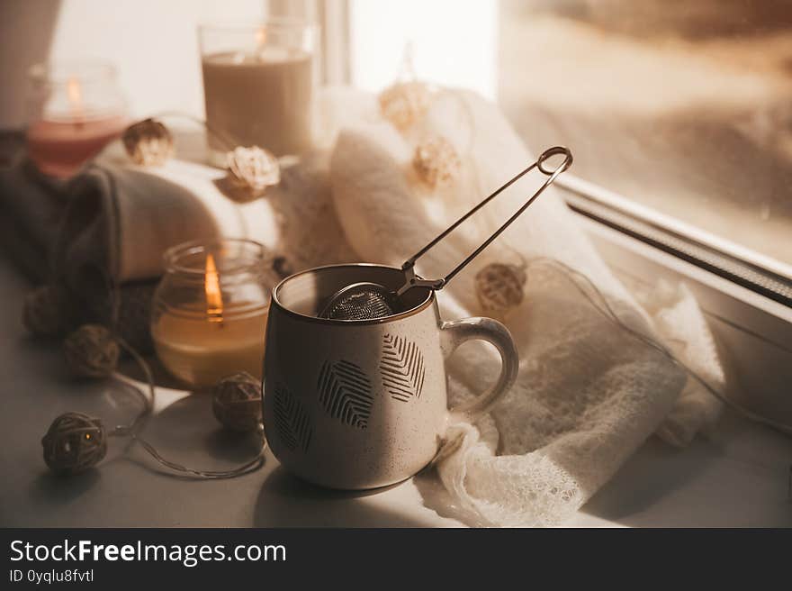 A cozy and warm hygge concept with white sweaters, candles, a cup, a garland on the windowsill. Autumn trends.