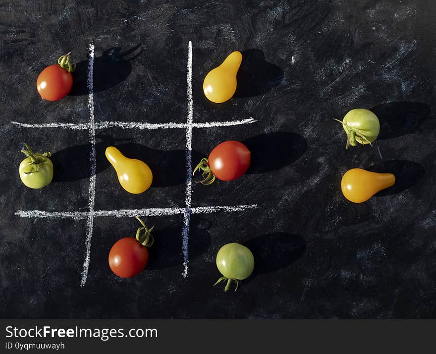 Multi-colored cherry tomatoes laid out on a dark background in the cells, drawn with chalk. Didactic game. Background with food