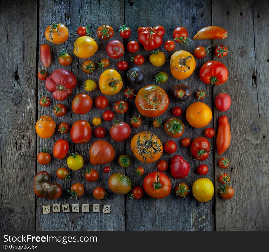 Tomatoes Of Different Varieties And Colors Top View. The Word Tomatoes Is Inscribed In Wooden Letters. Layout On A Wooden