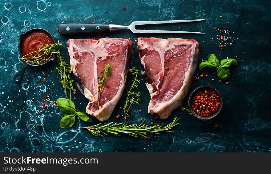 Dry raw two T-bone steak on the bone with spices on a black stone background. Top view. Rustic style