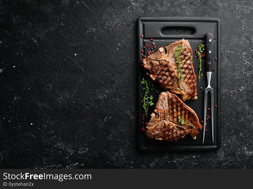 Two juicy grilled steaks with spices and herbs on a black background. Top view. Rustic style