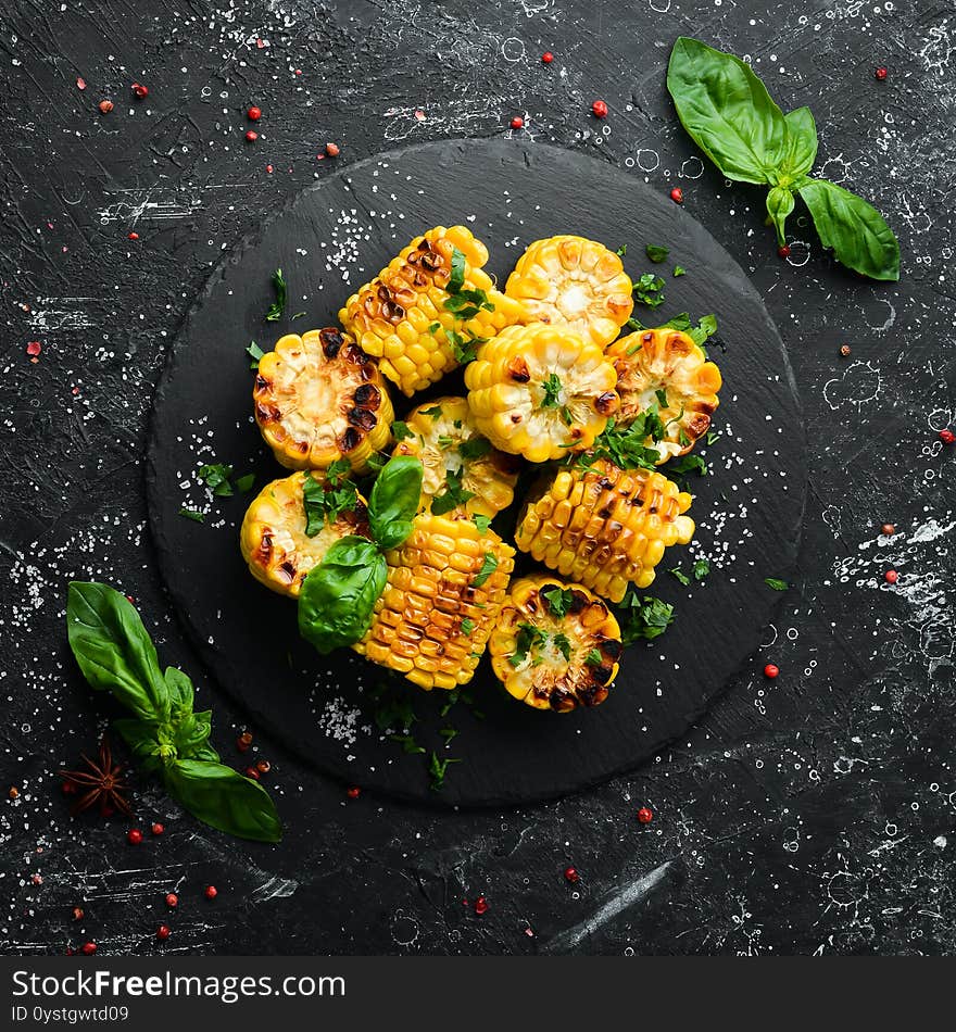 Food. Baked corn with parsley and basil on a black stone plate. Top view. Free space for your text