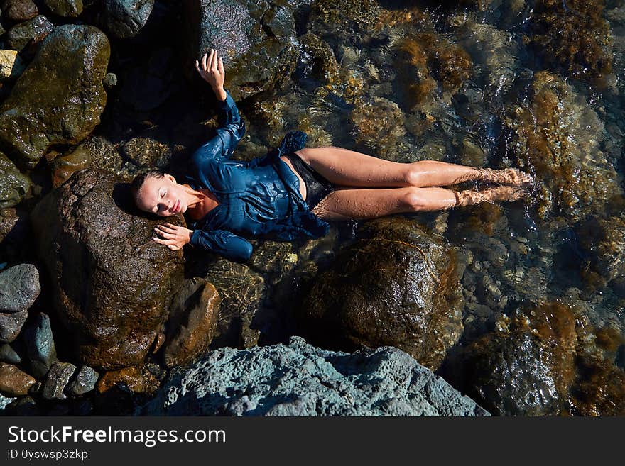 Female Laying On Sea Rock. Lady In Wet Blue Dress. Summer Time And Relax. Beach Vacation. Relaxation And Meditation