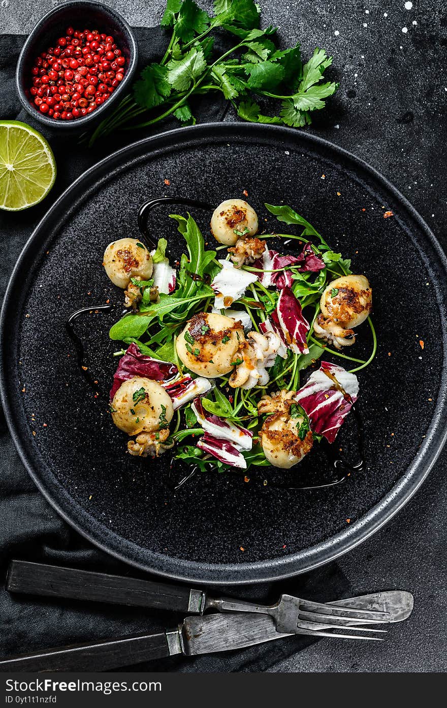 Salad with grilled cuttlefish and arugula. Black background. Top view.