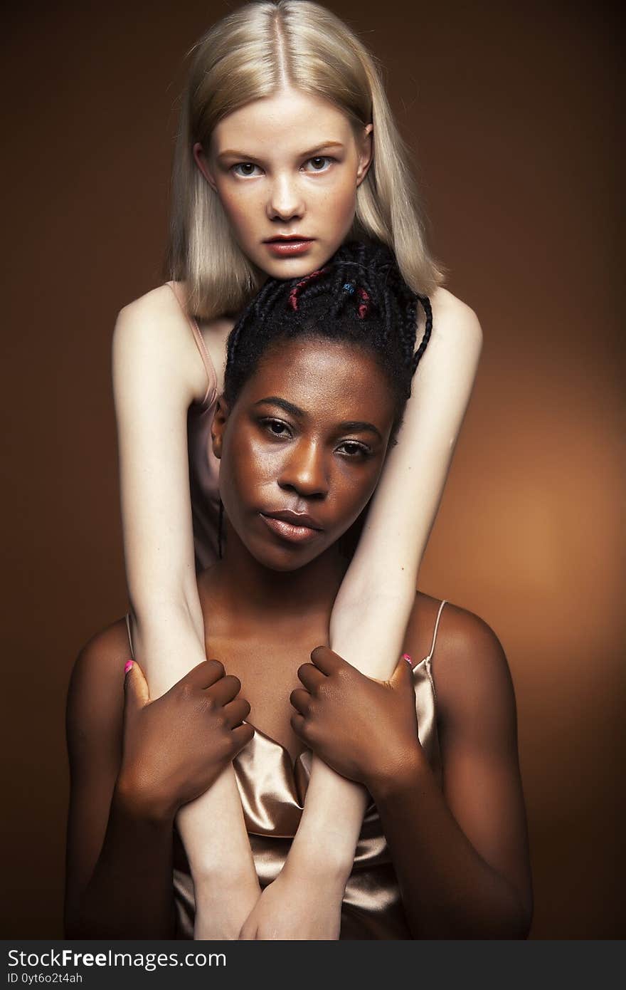 Two pretty girls african and caucasian blond posing cheerful together on brown background, diverse lifestyle people